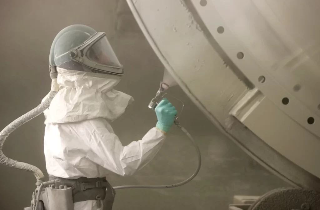Worker in PPE airless spraying large industrial tank
