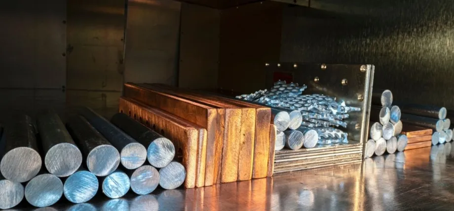 An assortment of non-ferrous raw materials, such as aluminum rounds and copper bars, arranged on a reflective metal workbench.