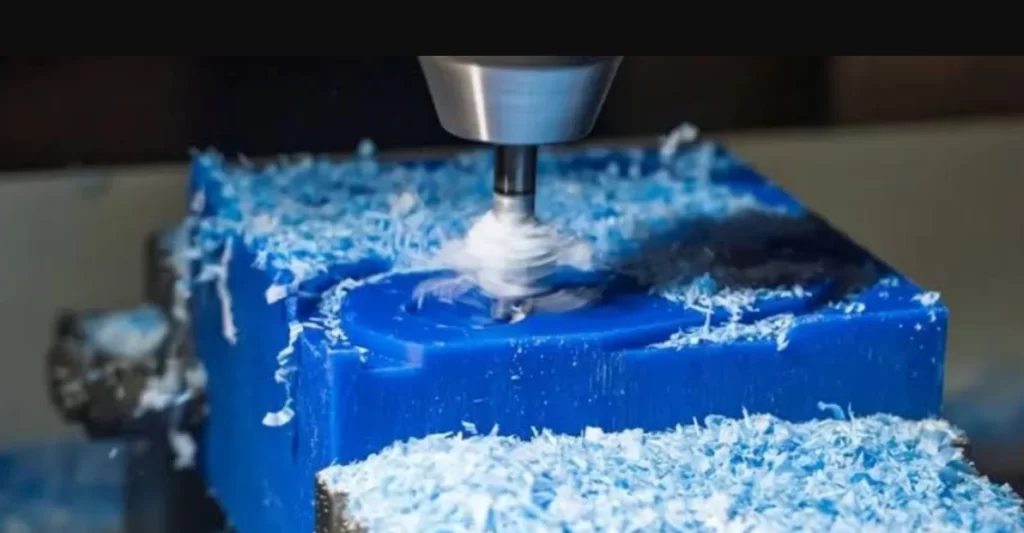 CNC end mill cutting a blue ABS block, producing curled plastic shavings.