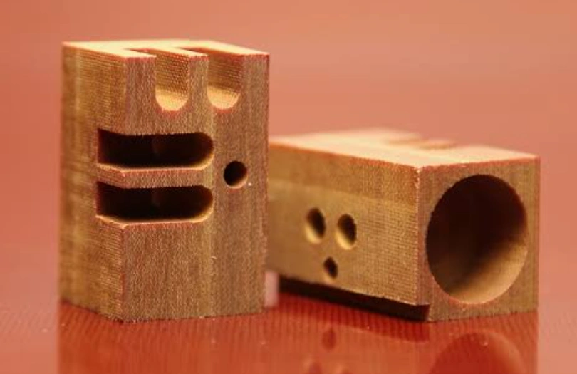 Two machined phenolic resin blocks with slotted and drilled hole patterns, showing a laminated grain texture.