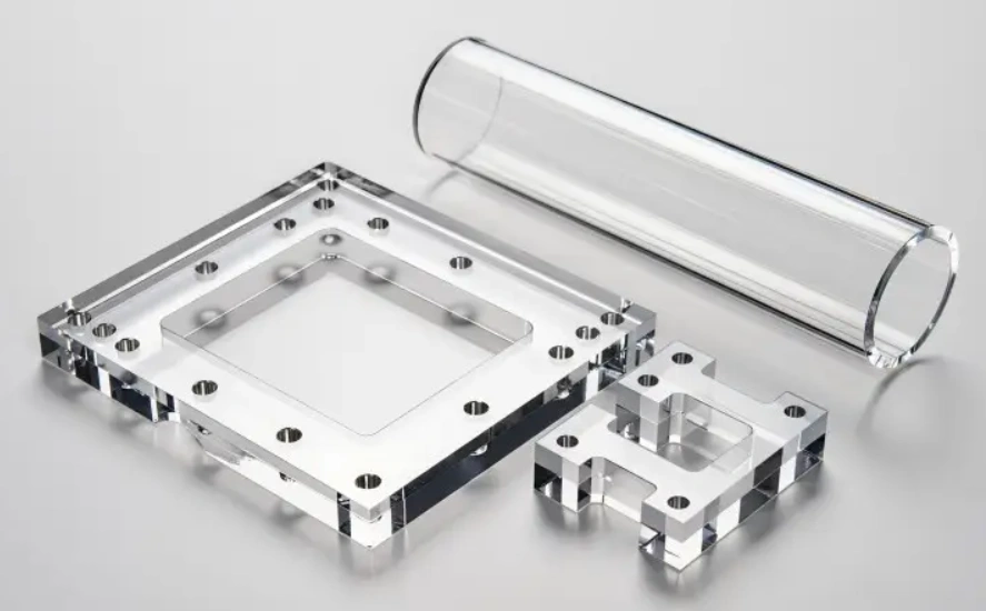 CNC-machined clear acrylic parts, including a square frame, bracket, and hollow tube.