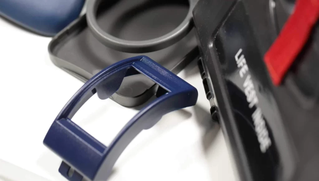 Close-up of injection-molded aircraft cabin components, including a blue tray table latch and black life vest instruction placard