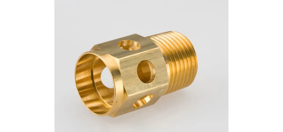 Machined brass fitting, likely alpha or alpha-beta brass type, with hexagonal body, external threaded ends, and multiple drilled cross-holes for fluid flow