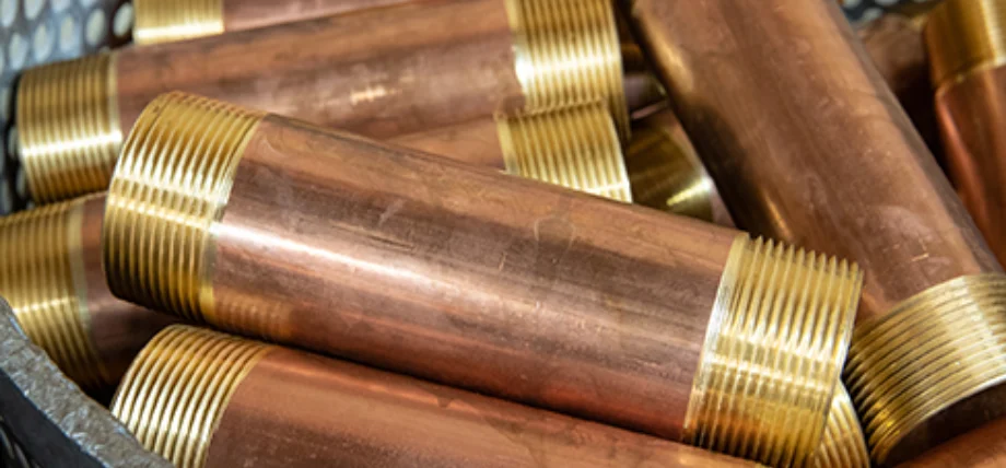 Pile of machined brass nipples and fittings with copper-toned bodies and bright gold-threaded ends, featuring detailed external threading.