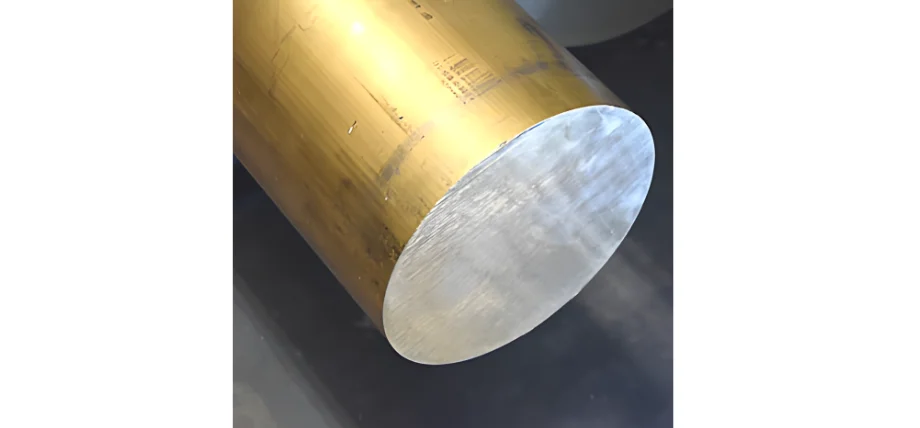 Close-up of a large cylindrical brass rod with a polished silver-gray end face and a golden-yellow oxidized surface showing machining marks.