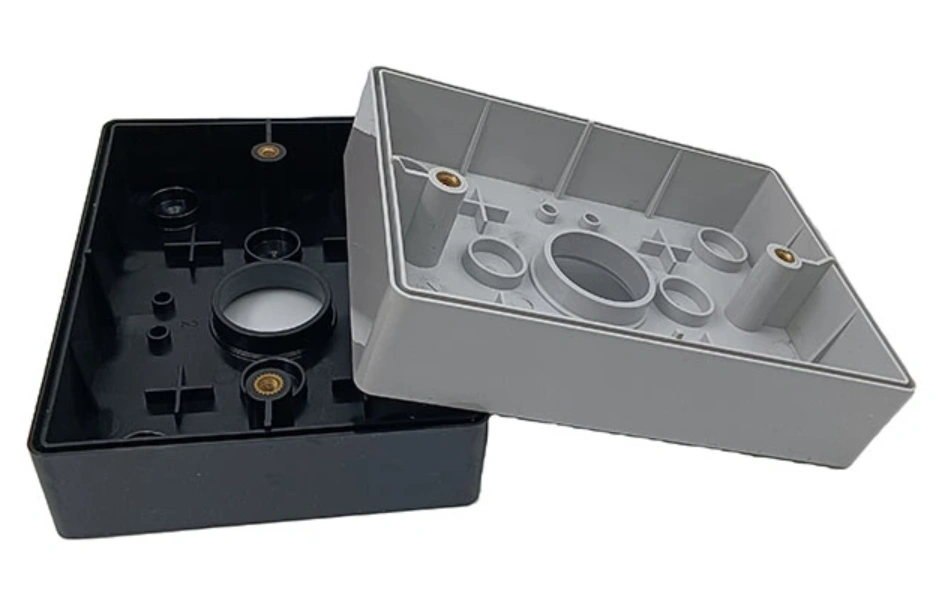 Black and gray injection-molded electrical junction box casings with cable entry holes and brass mounting inserts