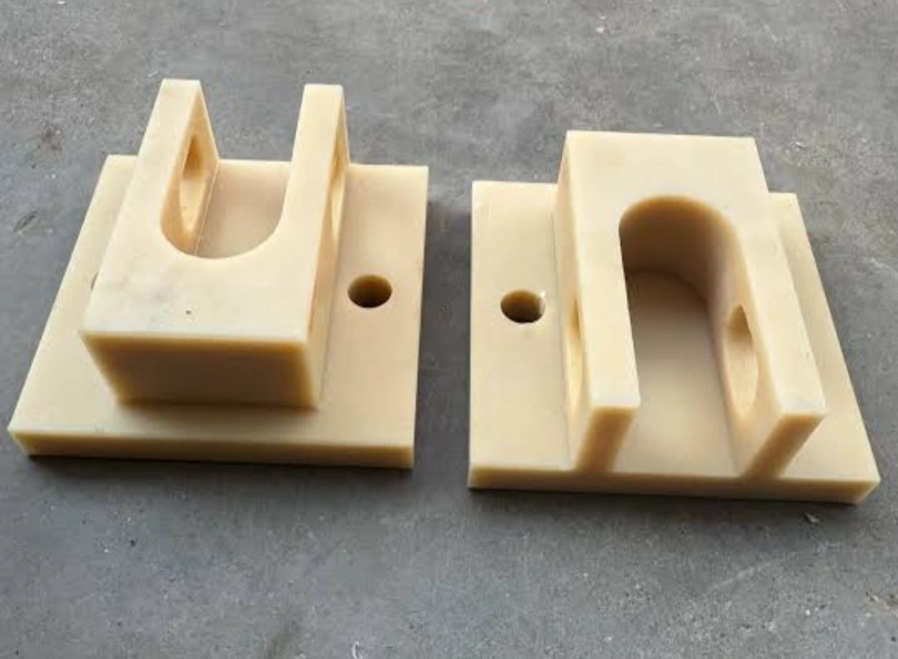 Two machined nylon (PA) mounting blocks with U-shaped cradle cutouts and bolt holes.