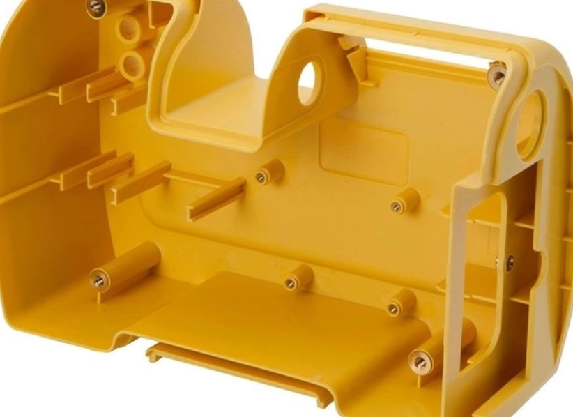 Complex yellow injection molded plastic part with multiple mounting bosses, reinforcing ribs, and curved wall sections.