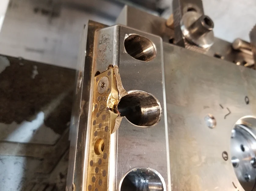 Close-up of a damaged steel injection mold block showing a cracked and broken corner near a cooling channel hole.