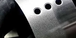 Preparing an Anodized Surface for Powder Coating A close-up of a metal part with three circular holes, showing a rough, sandblasted texture.