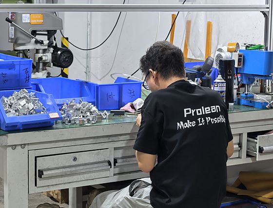 An operator in a Proleantech work shirt sorting machined parts into blue bins at a bench