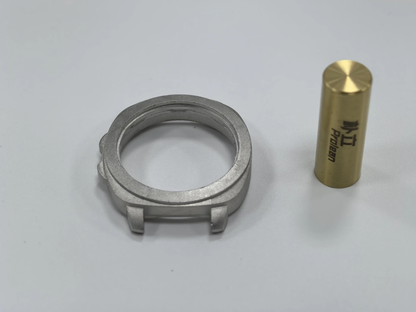 A metal ring with mounting features alongside a gold Prolean-marked reference cylinder