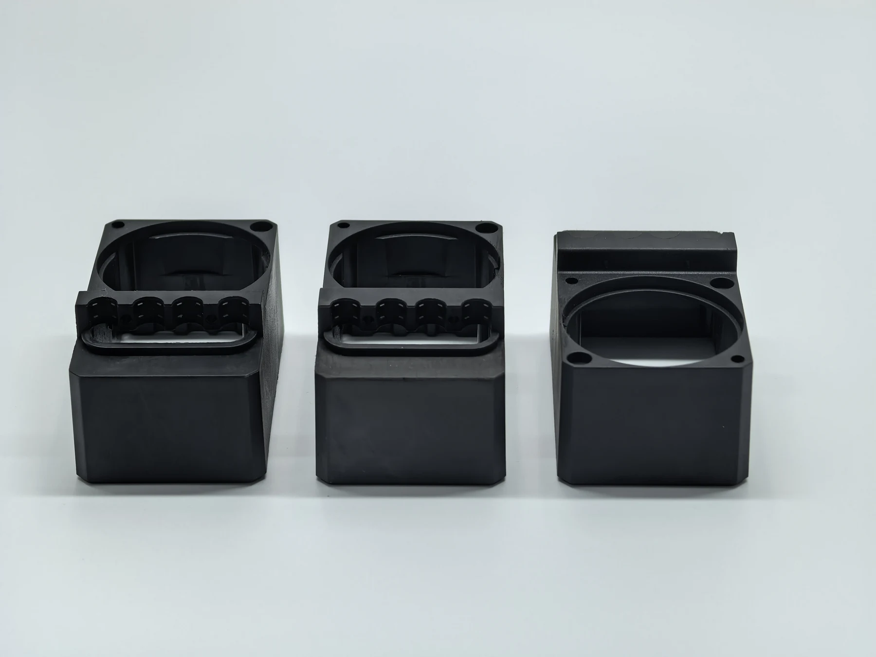 Three black machined housings with pockets and mounting features