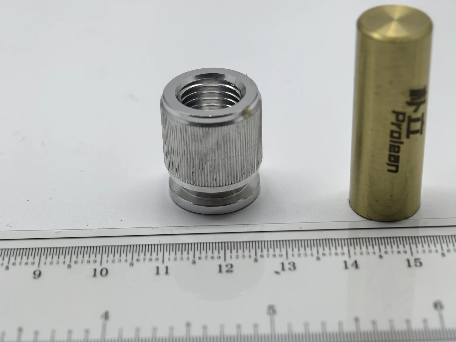 Threaded cylindrical metal component with an external textured band beside a ruler