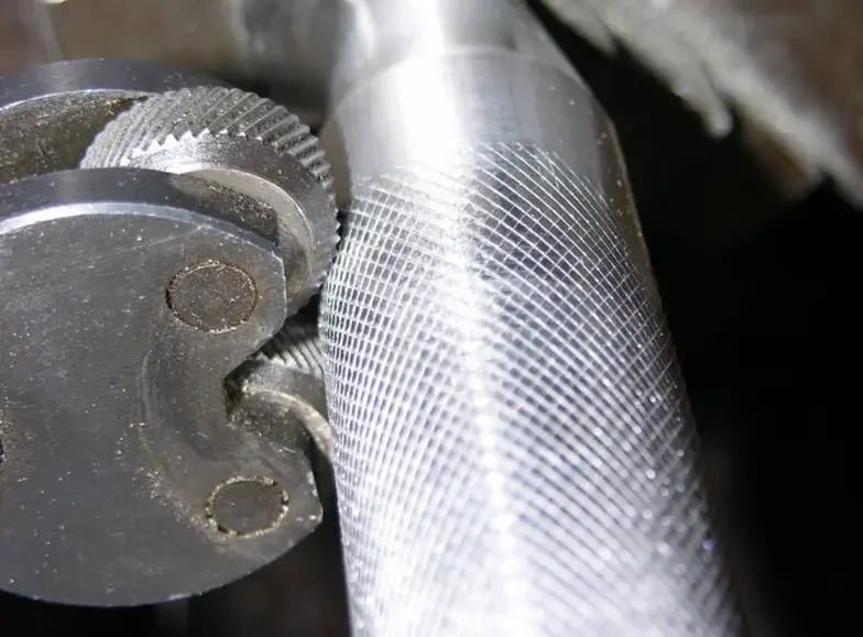 Two knurling wheels engaging a cylindrical workpiece with a diamond pattern