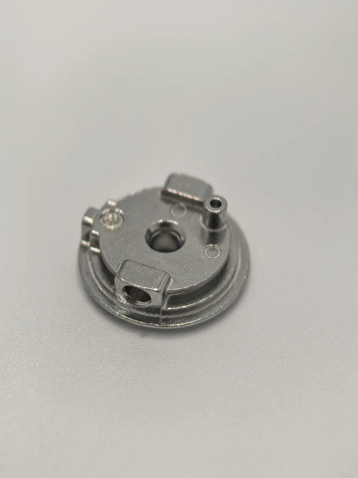 Compact finished MIM component with a central opening, side features and raised pin