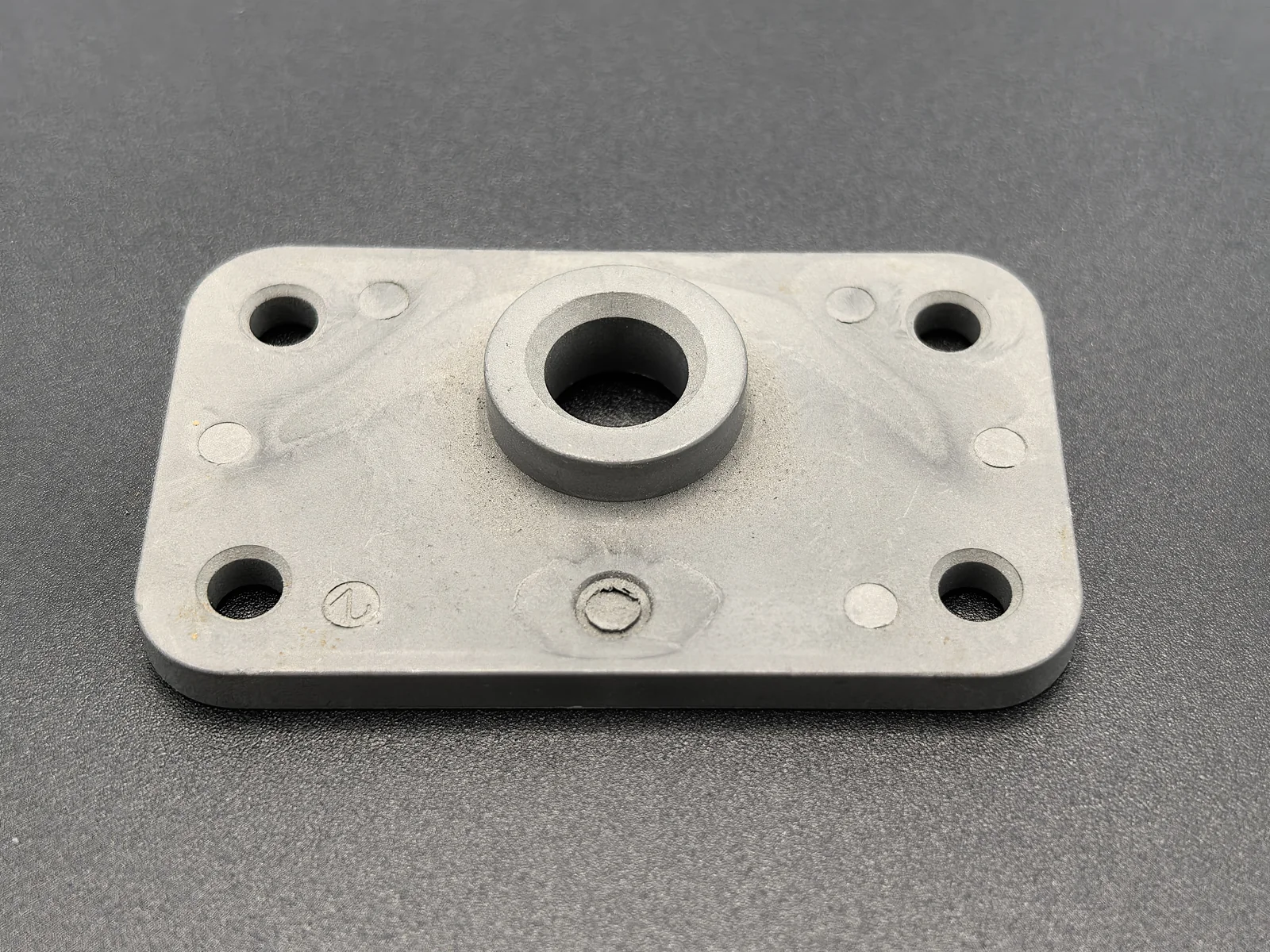Finished rectangular MIM mounting plate with four corner holes and a central raised boss