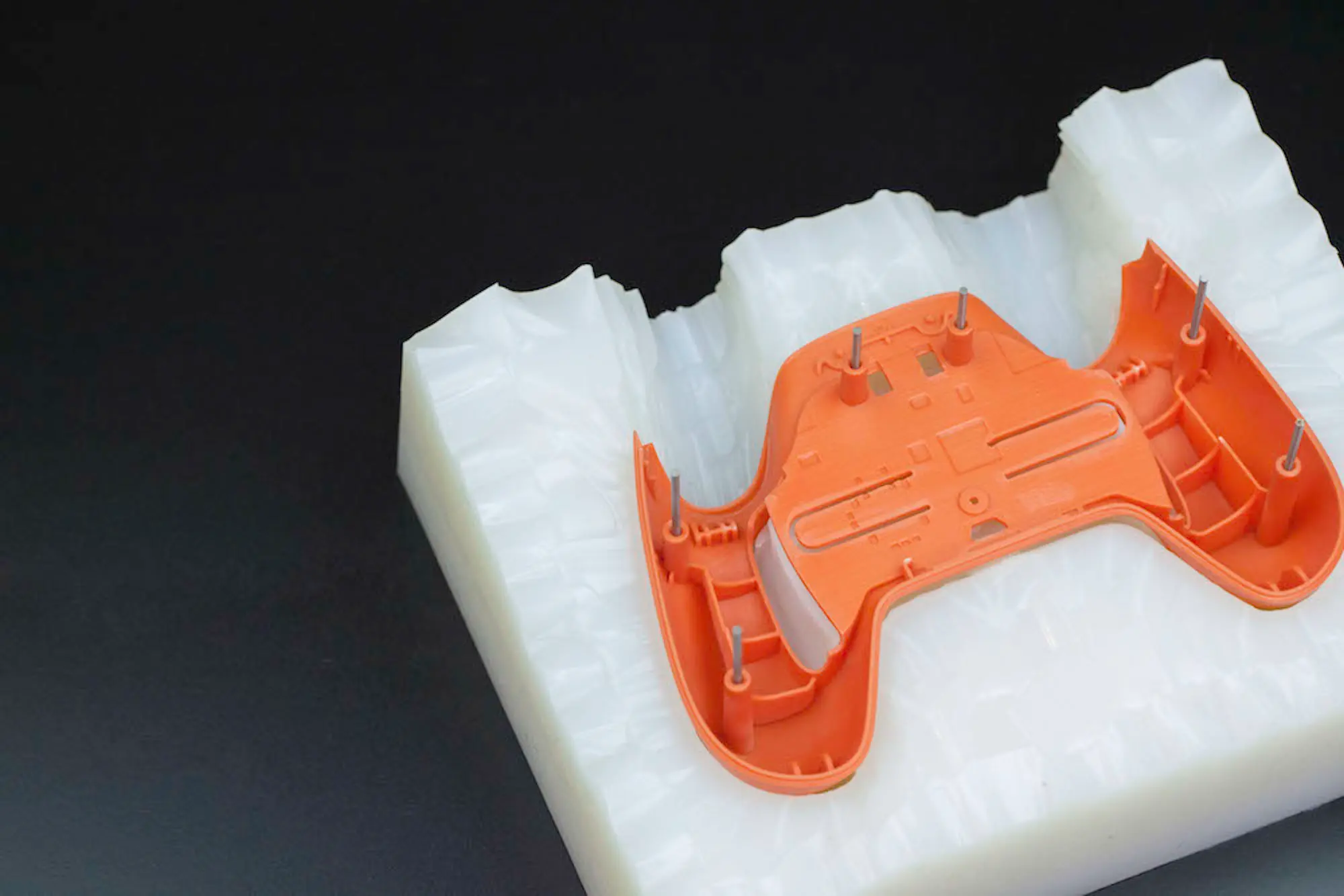Orange enclosure prototype seated in an open silicone mold, with ribs and mounting features visible